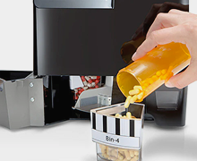 MedaCube with the restock door open, one bin pulled out and pills being poured from an orange pill bottle directly into the removed medacube bin 