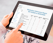 Hand holding a tablet showing a medication adherence report. 