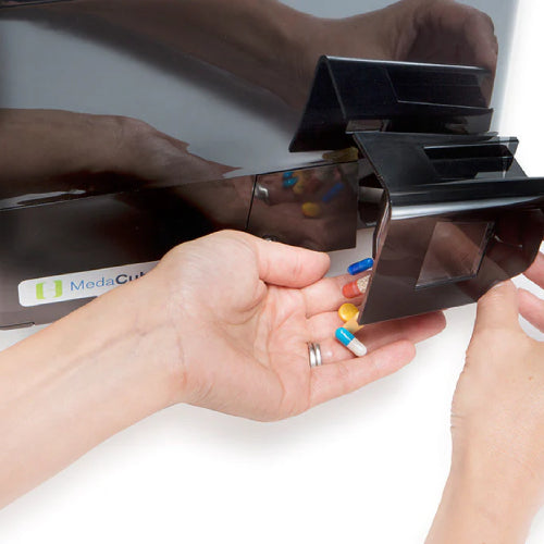 One hand tilting the dispense drawer of the MedaCube. Pills in the dispense drawer are poured into the hand that is not tilting the dispense drawer. Displays ease of use of the dispensing action. 